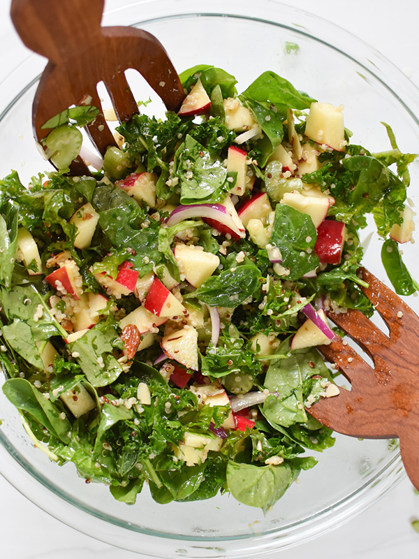 Salad with apples, quinoa and red onions in a glass bowl with wooden salad spoons.