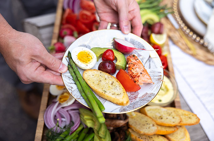 Plate with asparagus, sliced soft-boiled egg, garlic bread, olives, avocado slice, radish slice, and salmon.