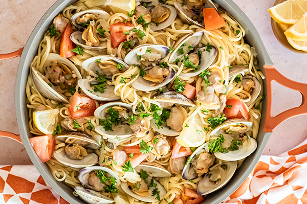 An overhead view of a pot filled with linguine pasta and clams, garnished with fresh herbs