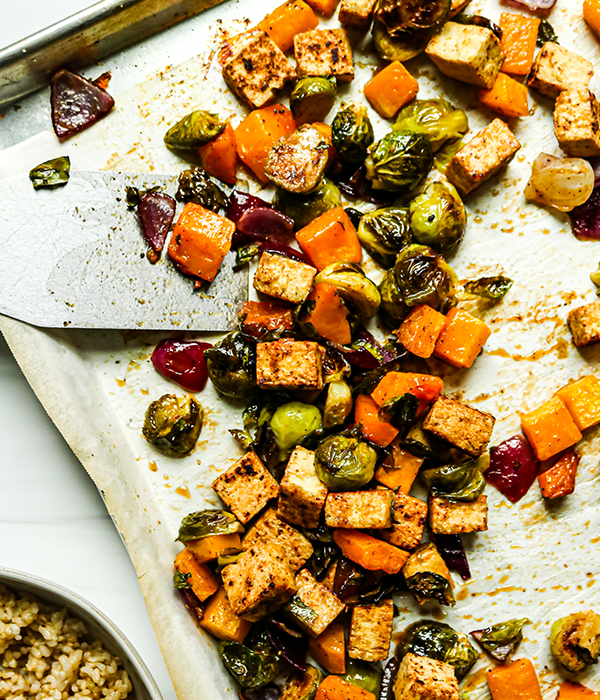 Crispy tofu with brussels sprouts, butternut squash, and red onion on a baking sheet.