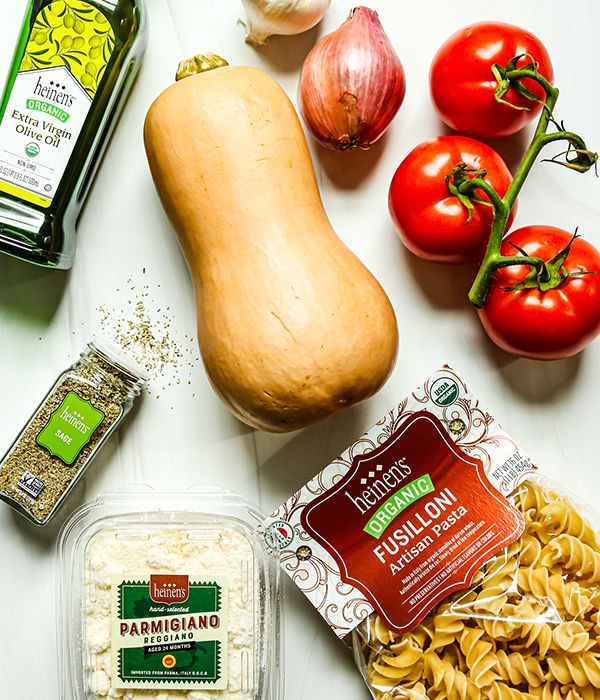 Butternut Squash, tomatoes, shallots olive oil, spices, parmigiano Reggiano, and fusilli pasta on a kitchen counter.