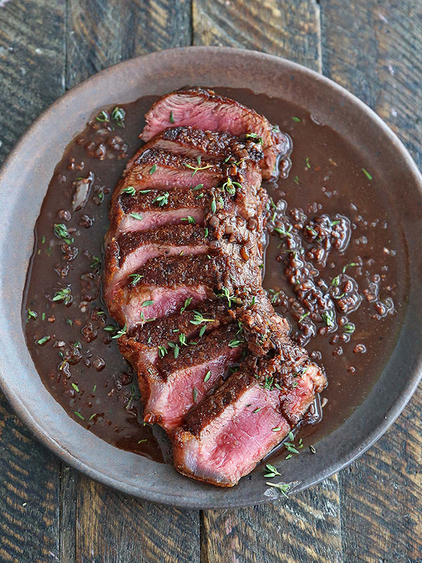 Sliced steak in a red wine brown sauce served on a plate.
