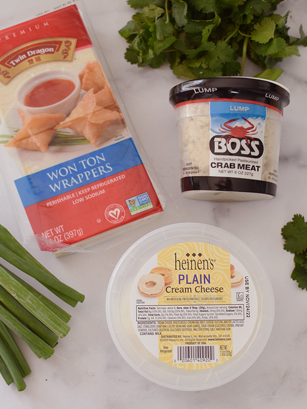Container with a package of wonton wrappers, container of Boss crab meat and Heinen's plain cream cheese, surrounded by chives.