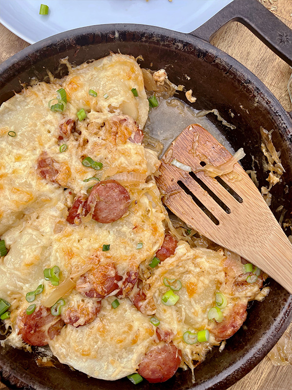 Pierogis topped with cheese, kielbasa and sauerkraut in a cast iron skillet.