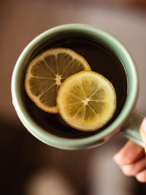 Overhead view of a green mug with hot tea and sliced lemons.