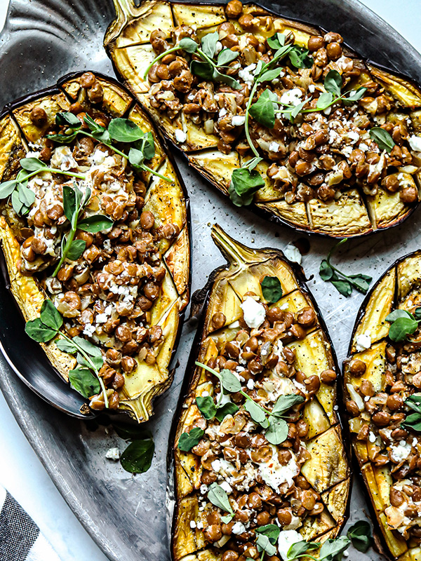 Eggplant stuffed with lentils, topped with goat cheese and microgreens, served on a plate.