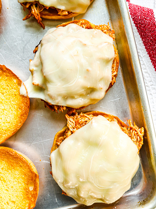 Shredded chicken parm sandwiches on a backing sheet with melted cheese.