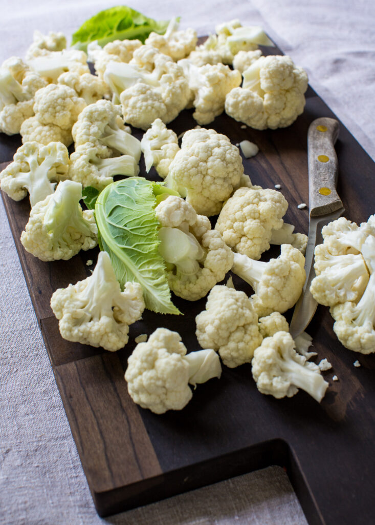 Cauliflower florets on a cutting board with a knife.
