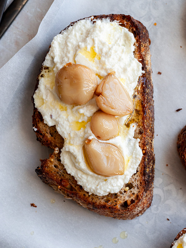 Toast with whipped ricotta and garlic confit on a baking sheet with parchment paper.