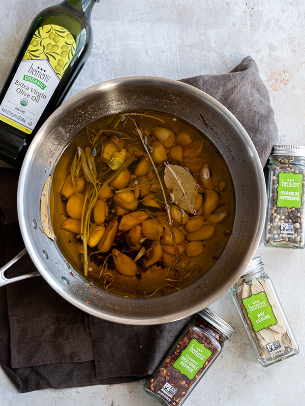 Pot filled with olive oil, garlic cloves bay leaves, pepper, and red chili flakes.