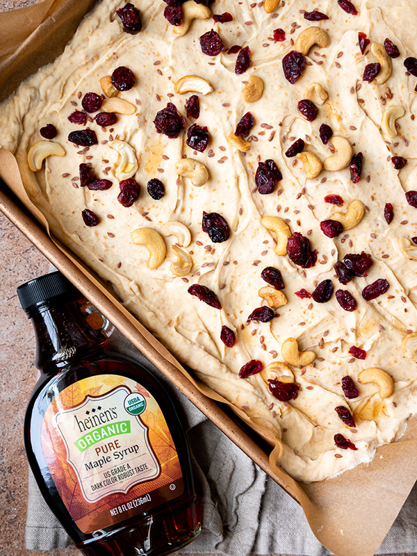Healthy Peanut Butter Yogurt Bark cut into squares and topped with raisins and cashews next to Heinen's organic maple syrup.