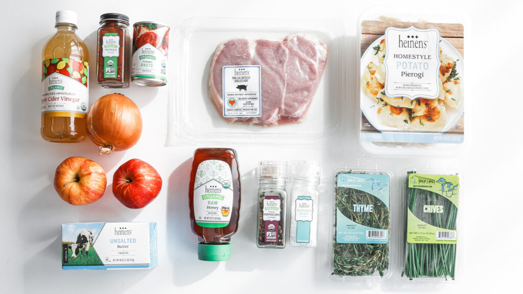 Spread of ingredients including pork chops, pierogis, apples, thyme, chives, a yellow onion, unsalted butter, tomato paste, apple cider vinegar and paprika.
