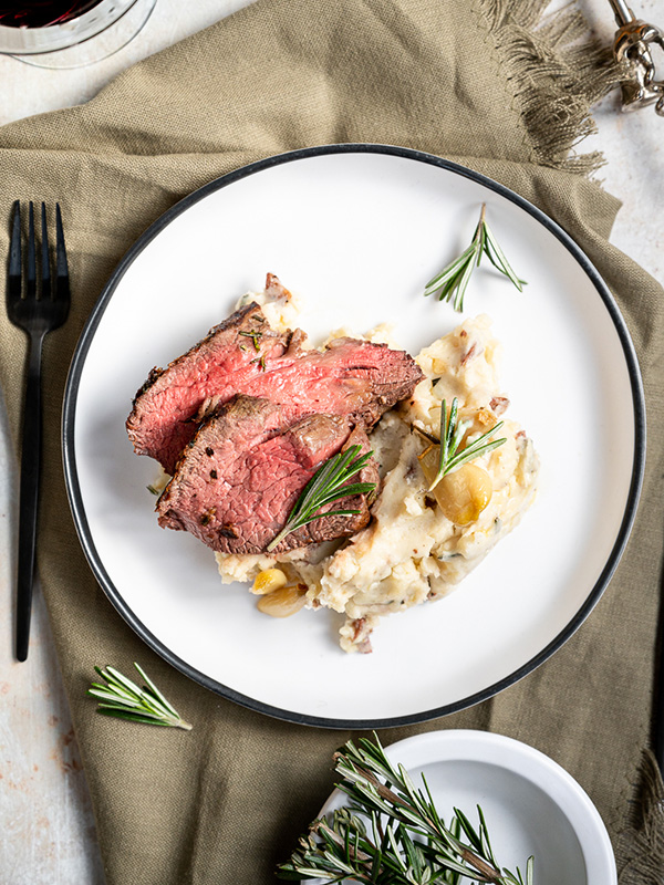 Plate with medium-rare beef tenderloin over garlic mashed potatoes.