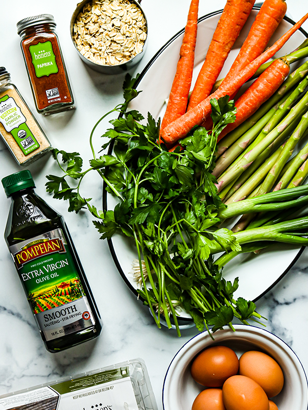 Plate with carrots, asparagus, leeks, and herbs next to olive oil, eggs, oats and spices.