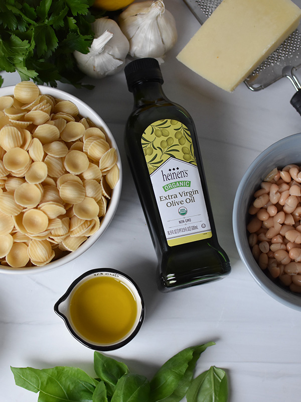 Cooked pasta in a bowl next to olive oil, garlic, parmigiano Reggiano and basil.