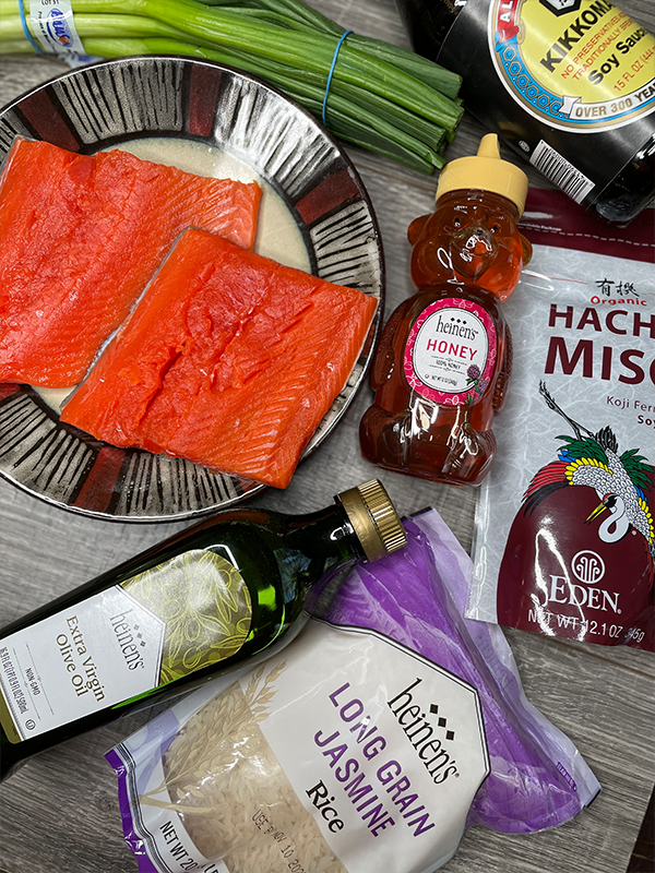 Fresh salmon on a plate next to honey, olive oil, jasmine rise, miso sauce, chives and soy sauce.