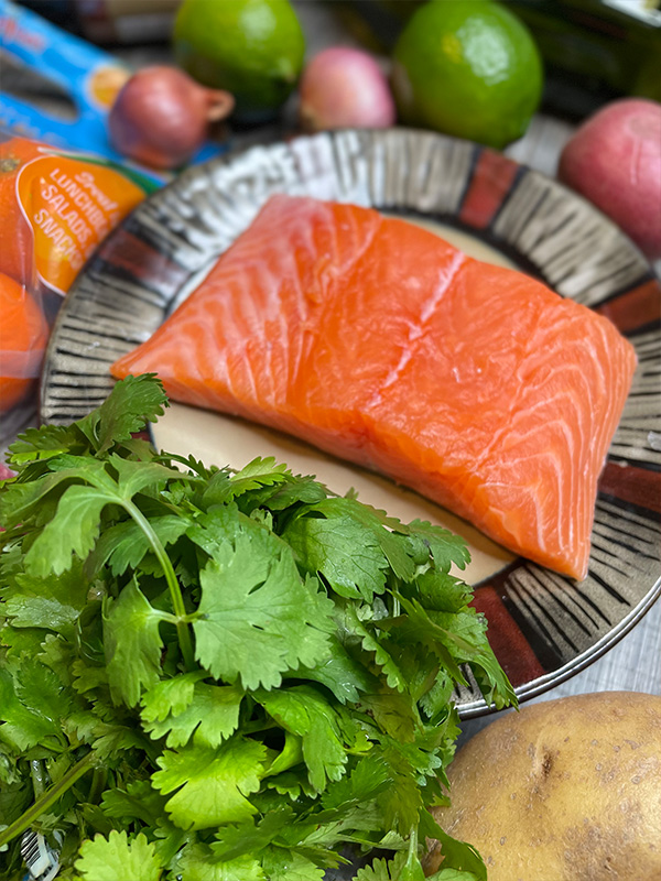 Fresh salmon fillet on a plate next to cilantro, limes and onions.