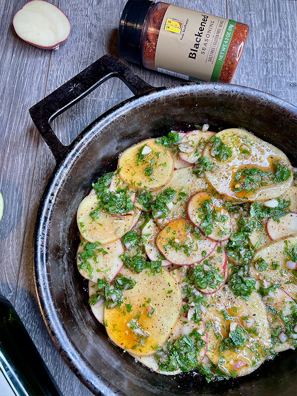 Thinly sliced red potatoes in a cast iron dish next to blackened seasoning.