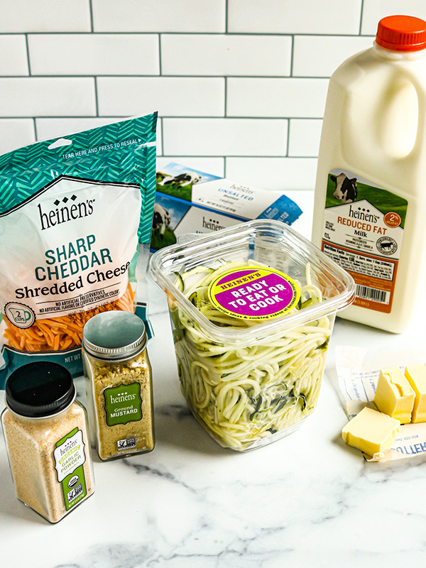 Spread of ingredients including ready-to-cook zucchini spirals, whole milk, butter, cheddar cheese, and seasonings.