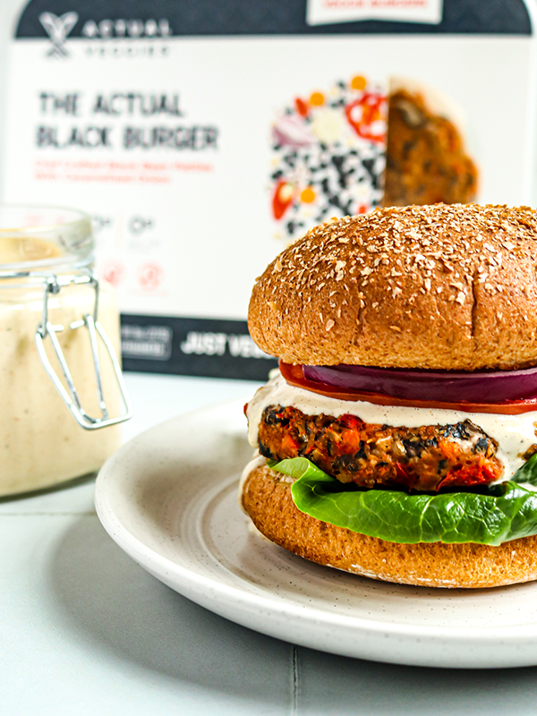 Black bean burger served on a bun with red onion, lettuce, tomato and sauce.