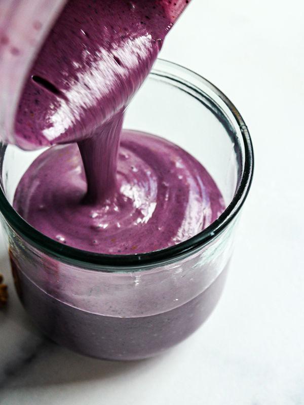 Purple smoothie being poured from a blender into a glass.