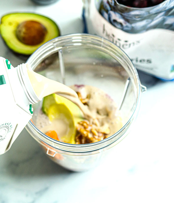 Overhead view of milk being poured into a smoothie container.