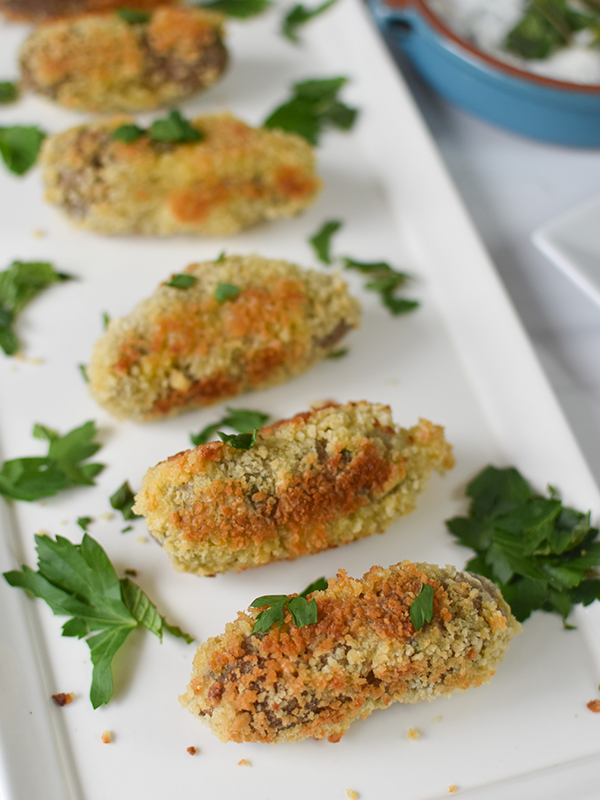 Lamb Croquettes in a row on a serving dish with herbs.