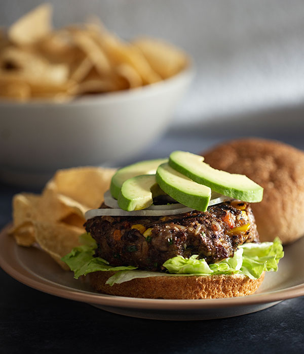 Heinen's Black Bean Burger on an Open-Face Bun with Sliced Red Onion, Avocado, and a Side of Tortilla Chips
