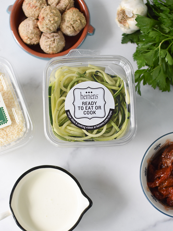Package of ready-to-eat zucchini noodles next to meatballs, garlic, cream, parmesan cheese and herbs,