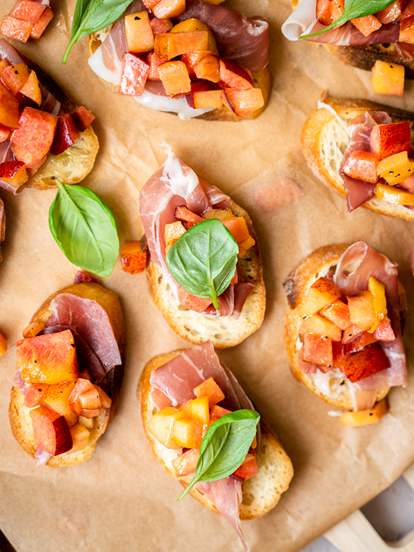 French bread slices topped with prosciutto, peaches and basil.
