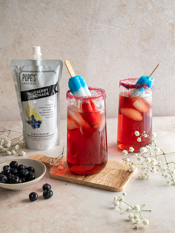 Glasses of blueberry lemonade topped with a frozen bomb pop popsicle and sugar rim.