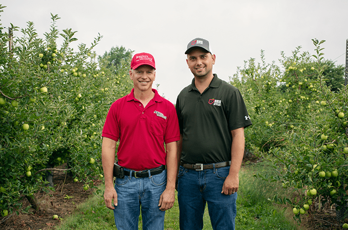 Two Farmers from Burnham Orchards Smiling in an Apple Orchard