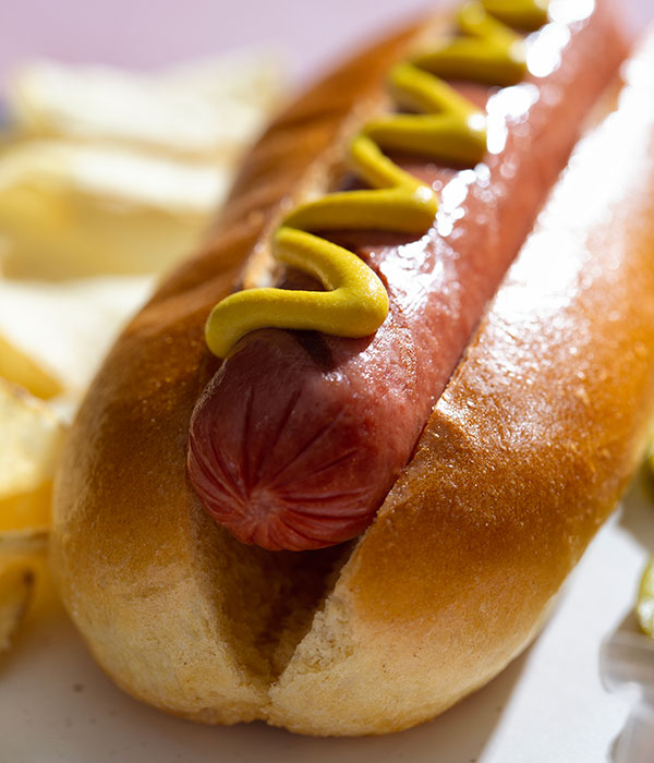 Hot dog in a brioche bun topped with yellow mustard.
