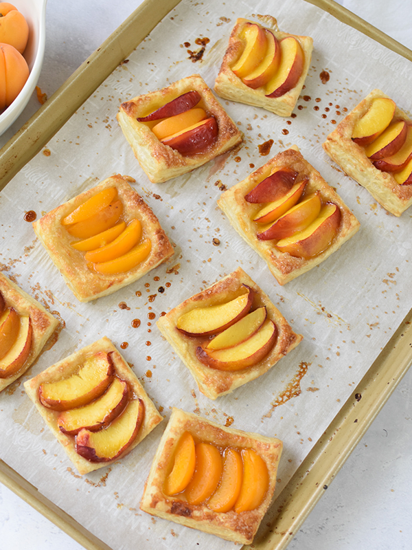 Stone fruits tarts on a baking sheet with parchment paper.
