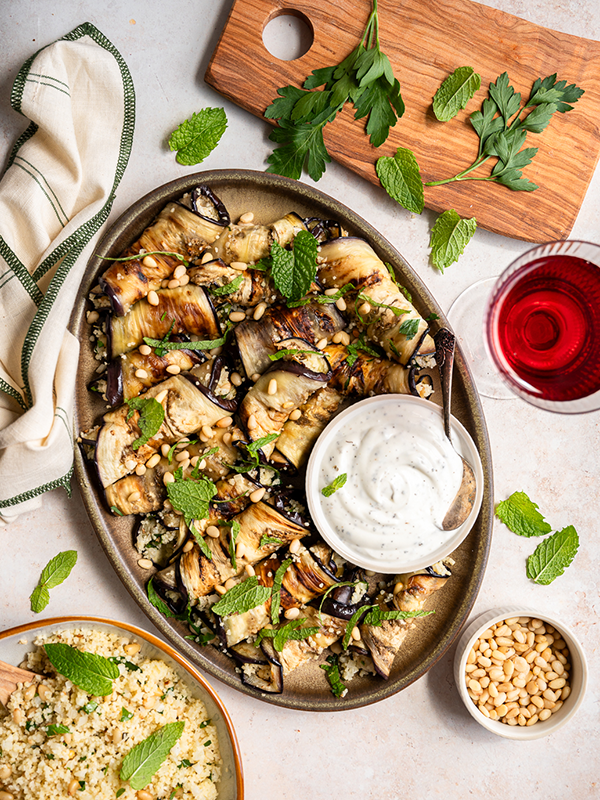 Couscous stuffed eggplant rolls on a serving dish with a white Italian dipping sauce.