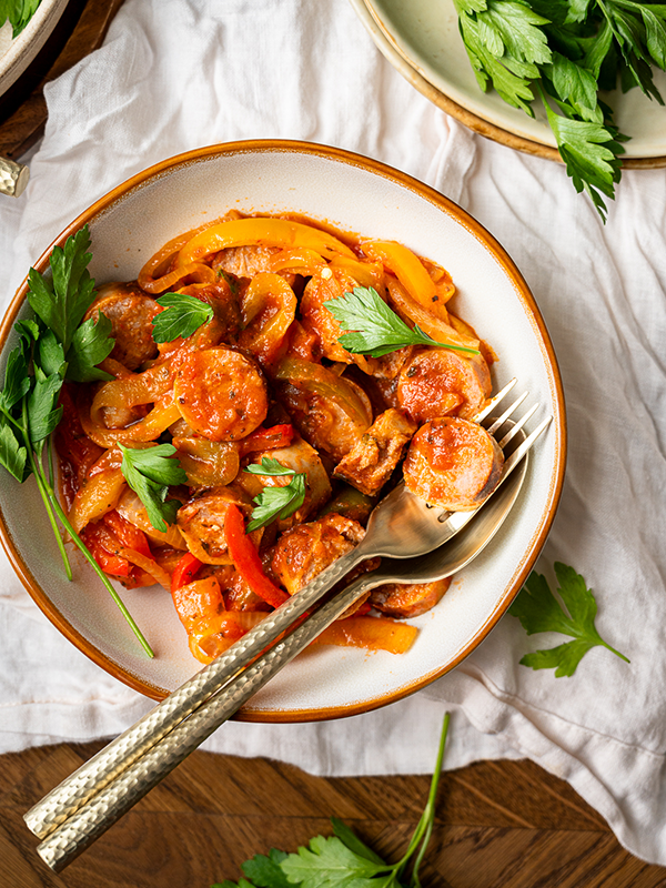 Sliced sausage and peppers with marinara in a bowl with a fork.