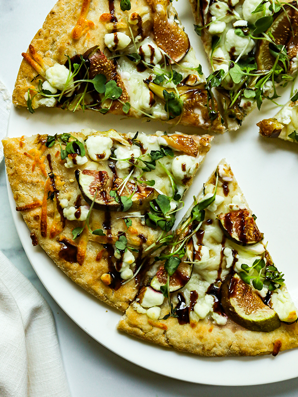 Slices of pizza on a plate topped with goat cheese, arugula, figs, and balsamic drizzle.