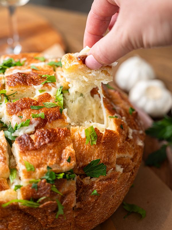 Whole bread loaf with square cuts on the top stuffed with cheese and herbs.