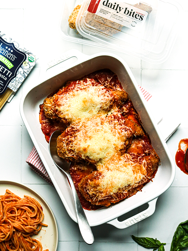 Breaded chicken in a baking pan with marinara sauce and cheese with a side of spaghetti with marinara sauce.