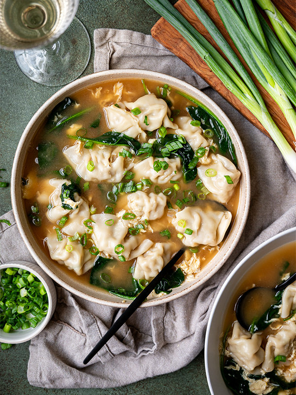 Egg drop soup in a bowl next to a cutting board with chives.