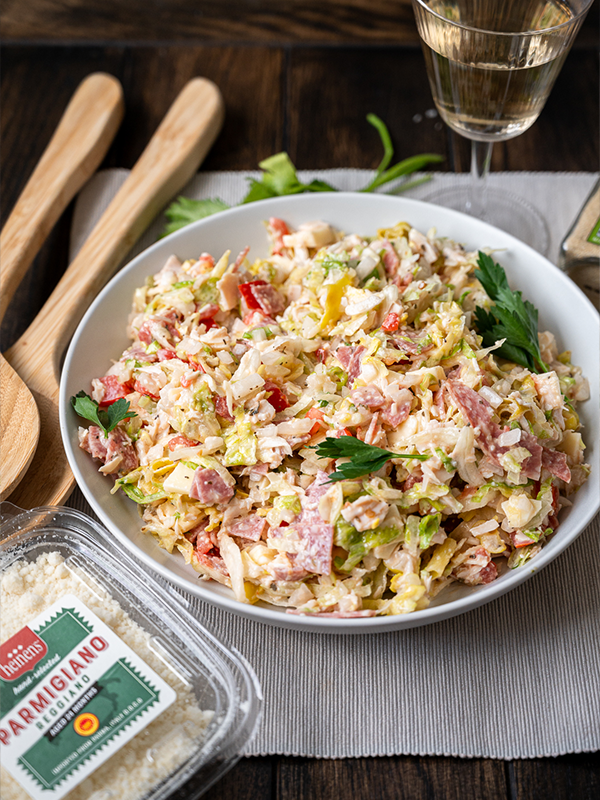 Grinder salad in a serving bowl next to fresh Parmigiano Reggiano.
