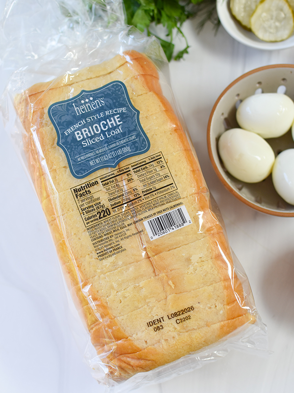 Loaf of Heinen's sliced brioche bread next to a boil of hardboiled eggs and pickle slices.
