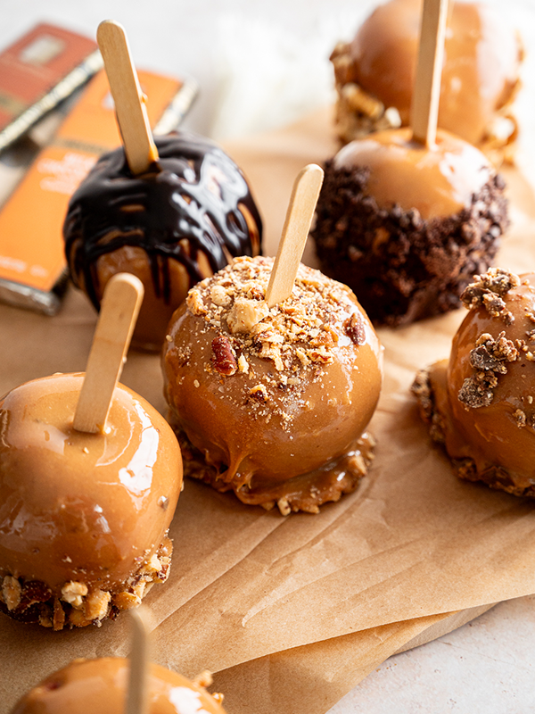 Carmel apples arranged on parchment paper and topped with nuts and chocolate.
