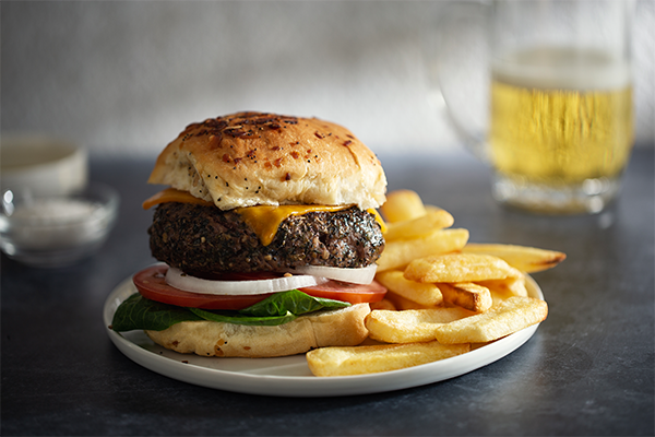 Heinen's gourmet burger on an onion bun with cheese, onion, tomato and lettuce with a side of French fries.