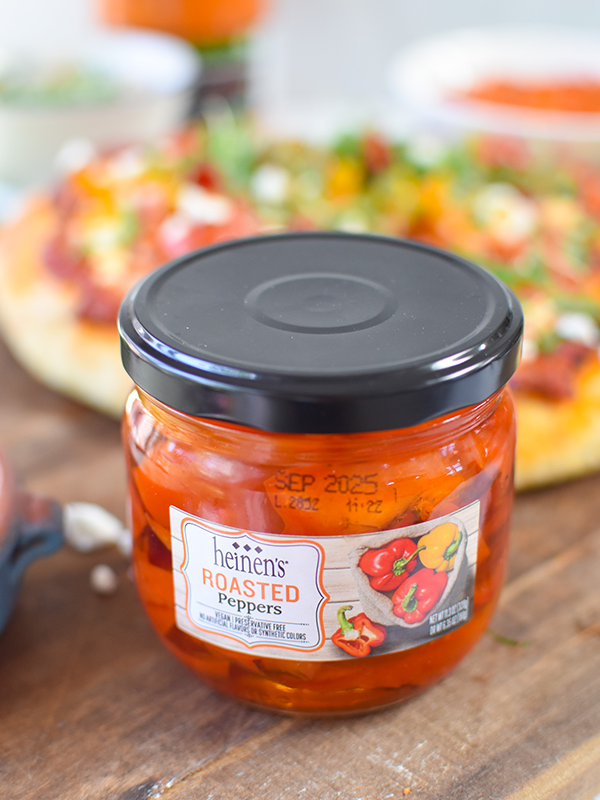 Jar of Heinen's roasted peppers on a cutting board with pizza.