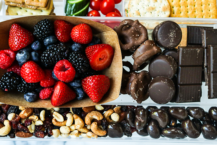 Snackle Box with mixed berries, an assortment of chocolate, trail mix, cucumbers, tomatoes, and crackers.