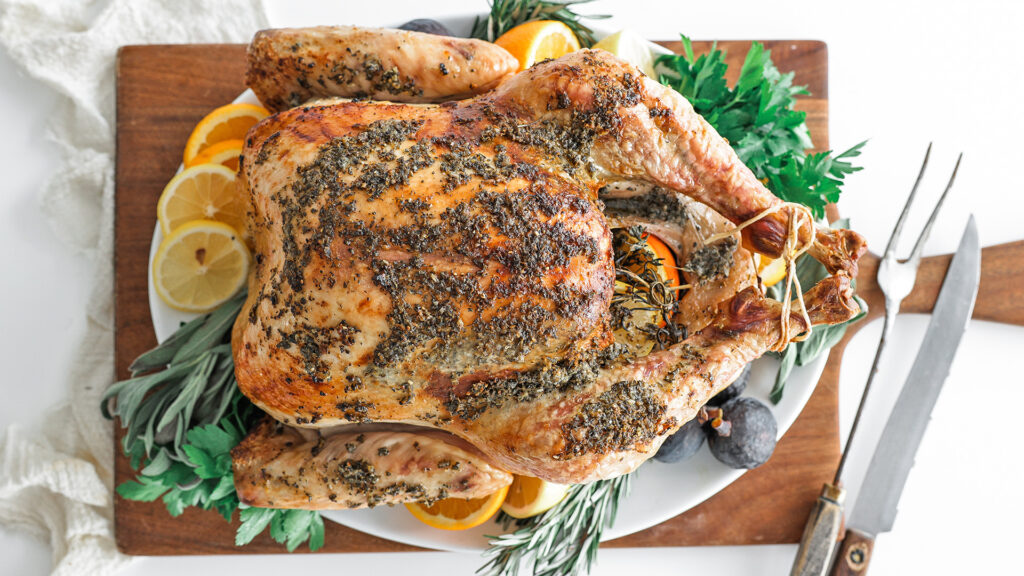 Cooked whole turkey placed on a cutting board with fresh herbs and citrus fruits.