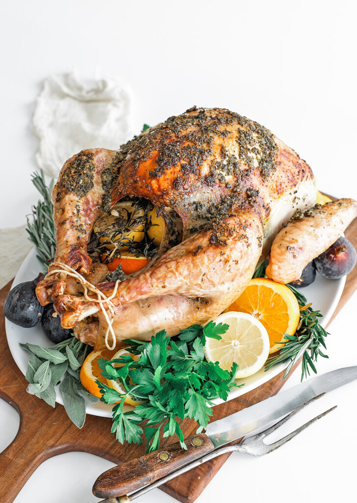 Whole cooked turkey on a plate with herbs and lemons.