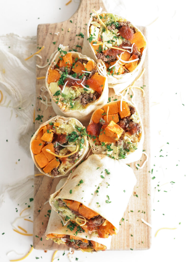 Breakfast burritos with egg, bison and sweet potato sliced in half and arranged on a cutting board.