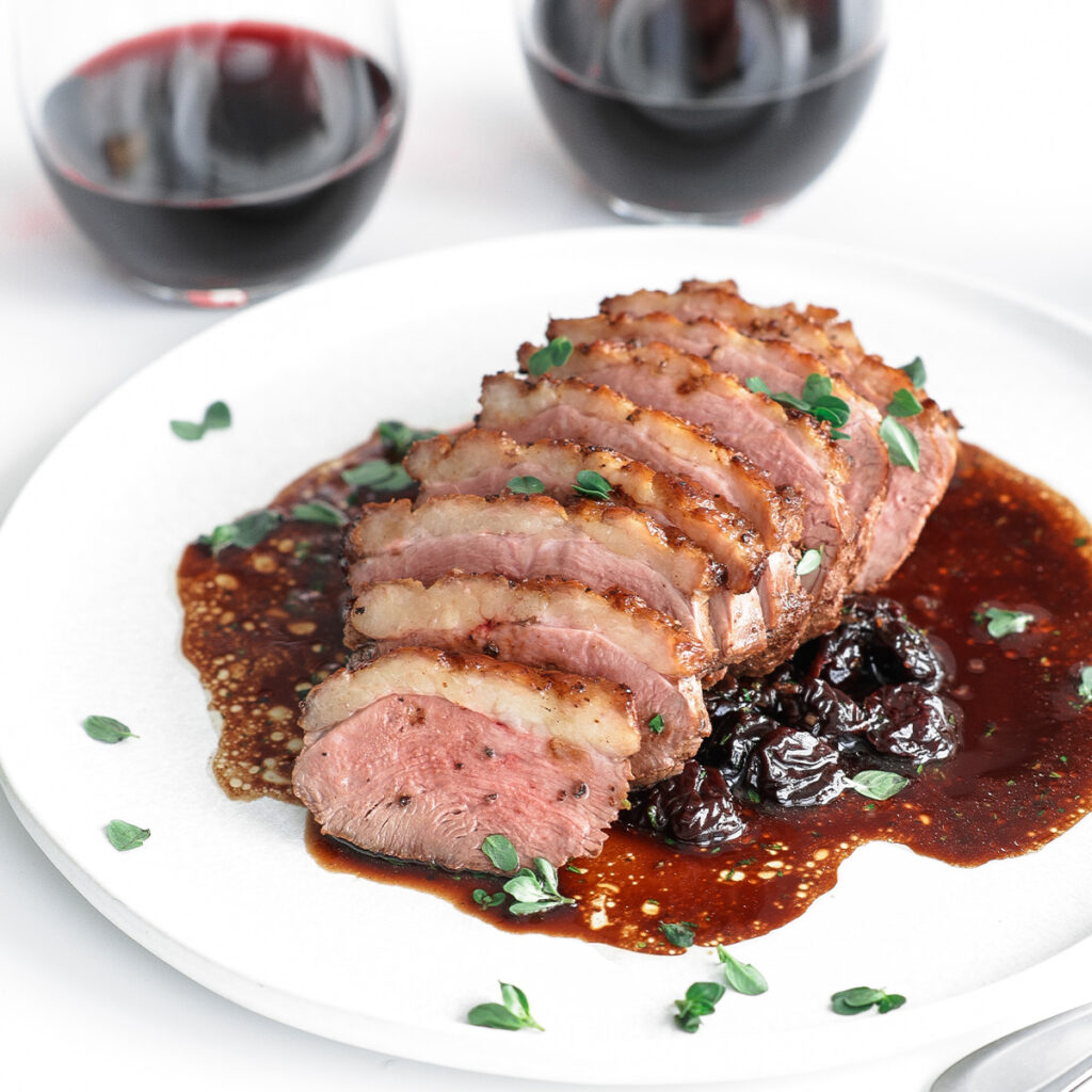 Duck breast served on a plate with cherry sauce and a glass of wine.